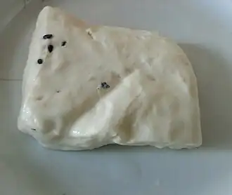 A solid block of white cheese with a smooth surface, with a few nigella sativa seeds embedded into it