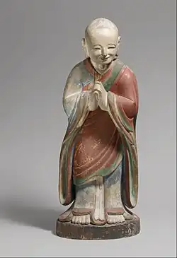 Monk in Chinese-style robes, bowing in respect with hands clasped and smiling