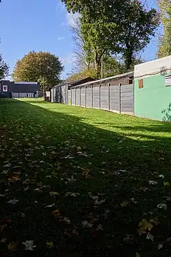 A 100yard outdoor shooting range stretches away. The range is grass, with a large brick structure and targets in the distance. A block building on the right han side of the range is painted green.