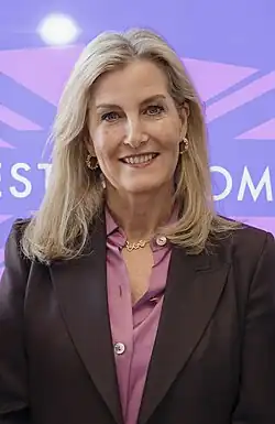 Sophie is smiling and wears a pink blouse and brown/burgundy coat.