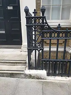 Metal railings around the same factory building, with a design showing a V, J and F