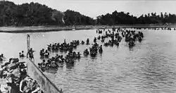 British soldiers wading ashore from landing craft. In the background is a tree lined beach
