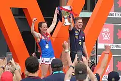 Pearce holding a large trophy alongside her coach