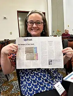 Image of woman holding a journal open to an article, conference attendees in the background