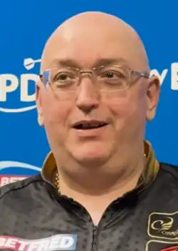 Andrew Gilding at a 2025 World Matchplay press conference, sitting in front of a panel with logos