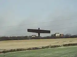 Statue viewed in the distance across fields. Railway overhead power lines can be seen in the immediate foreground