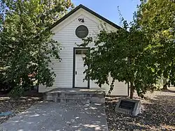 A white building with green trim, partially obscured by trees.
