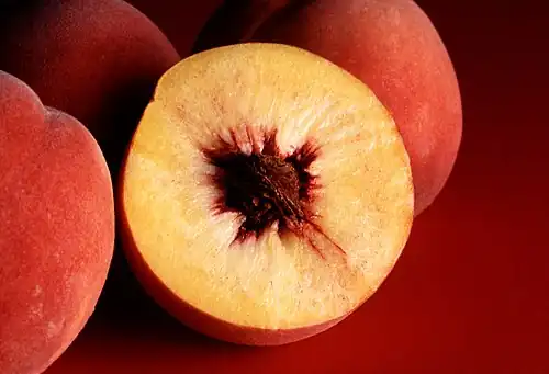 Photograph showing a peach in cross section with yellow flesh and a single large reddish brown pit