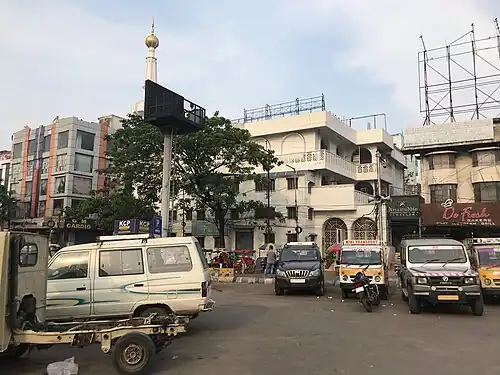 A white multi-storied building with one minaret, with a busy street in the foreground.
