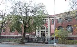 A two-story red brick building partially obscured by a tree on a cloudy day