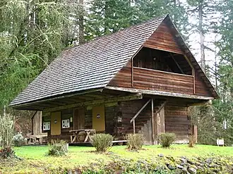 Photograph of a two-story log cabin, with an extreme overhang of the second story over the first