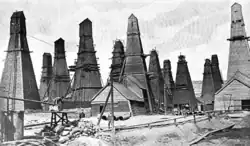 A black-and-white photograph showing a field of derricks each completely enclosed within its own oddly shaped wooden building.