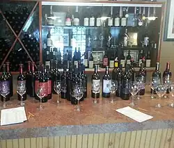 Rows of wine glasses and wine bottles on a bar, with a glass cabinet in the background displaying awards.