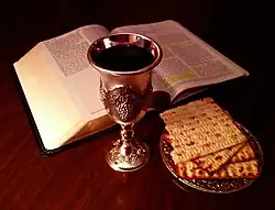 A Bible, a wine goblet and a plate of unleavened bread on a table