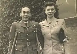 black and white photograph of a black man using crutches standing next to a white woman. Both people are wearing uniforms