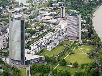 From left to right: a tall highrise, a rectangular complex of small white buildings and another smaller highrise photographed from above. They are in very close proximity of each other.