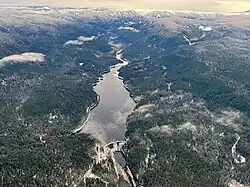 A large concrete dam impounds a lake surrounded by tree-covered hills.