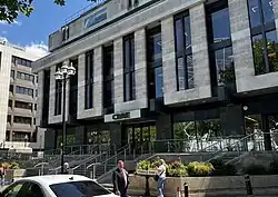 The image shows a grey office building with black windows and a car on the bottom.