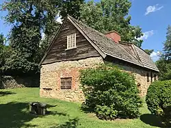 View of house from SW showing central location of chimney and transition in roof style from gable to gambrel, 2023
