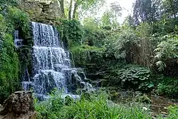 A colour photograph of an artificial waterfall surrounded by rocks and plants