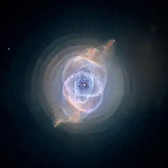 Blue-green diffuse disk with complex circular structure in its center. The disk is crossed by s-shaped brown curve.