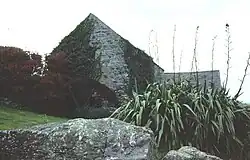 a stone building with a water wheel, rocks and plants in the foreground