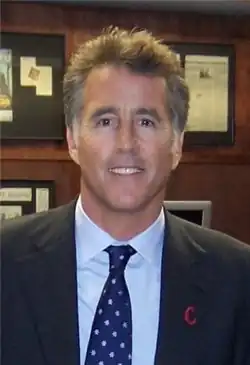 A middle-aged man, wearing a dark blazer, light-coloured shirt, and a blue and white tie.