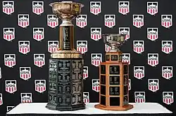Two large trophies sitting on a table in front of a backdrop with multiple instances of the USHL logo
