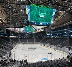 Interior view of an arena, featuring two big screens hanging above an ice rink