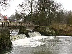 A stone footbridge crossing a weir, which is in a heavy flow state