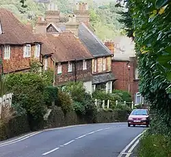 steep road with car passing a row of old red brick and tile-hung cottages