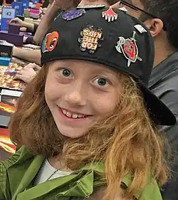 Head and shoulders of Fischer, an eight-year old girl with reddish blonde hair in a black baseball cap and green costume