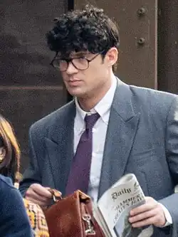 Clark Kent actor David Corenswet during filming in 2024, wearing glasses and a suit while carrying a newspaper and a briefcase