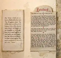 Two stone tablets of similar height set on a plain wall, both with black writing in an elaborate hand. That on the right also has the title "Exodus" in larger red writing, and several words are picked out in red.