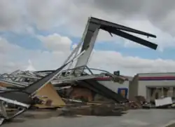 A white-and-red collapsed building with a large portion of wall sticking out of the ground above the rest of debris.