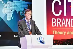 Dr. Keith Dinnie speaking at a podium during the 3rd 21st Century Maritime Silk Road Forum in Zhuhai, China, with a background screen displaying a world map and the words "City Branding: Theory and Cases"