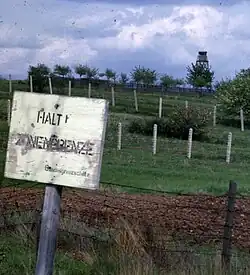 The "second-generation" fences in 1962, with derelict barbed wire in the foreground, a control strip, two rows of barbed wire further back and a watchtower at the rear