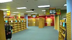 In the background are a number of empty shelves that are roped off. Signs hanging from the ceiling read "Entire store 80-90% off! STORE CLOSING". In the foreground, a person carrying a handbag is browsing the last few remaining books.