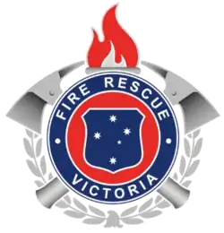 From a small silhouette of a brass firefighter's helmet rises a laurel wreath. Above it sits a shield of the Southern Cross, as in the Victorian coat of arms, encircled by the words FIRE RESCUE VICTORIA; behind this two crossed axes. A flaming torch surmounts the badge.