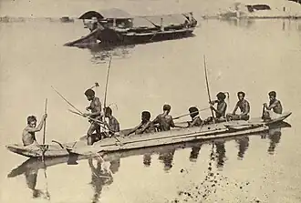 A small thin outrigger boat with nine men, some holding bows and arrows