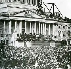 A large crowd in front of a large building with many pillars.