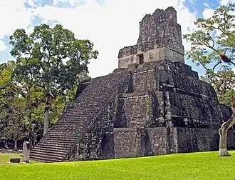 a steep-sided, stepped pyramid with a central staircase that rises from a flat, grassy area to a temple doorway at the top