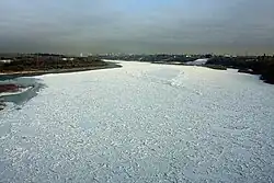 The surface of a wide river approaching a city is almost completely frozen.