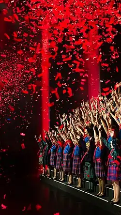 Cast memebers sing as red confetti showers down on them