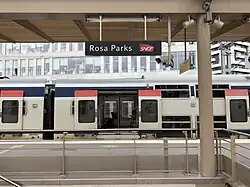 A photo of a railway station with a train passing by. The sign says Rosa PArks SNCF