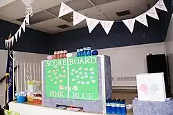 Room showing a multicolored scoreboard divided between "Team Pink" and "Team Blue" for a gender-reveal party.