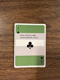 An ace of clubs with the words “GRAY ASEXUAL AND GRAYROMANTIC PRIDE” on it and grayromantic flag colors in the background, part of a display for International Asexuality Day set up in Pennsylvania in 2025.