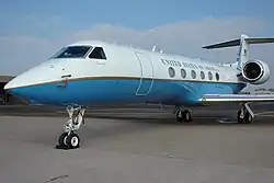 Small jet aircraft built by Gulfstream Aerospace; private executive versions are branded the Gulfstream V, and the Federal Government-owned version depicted here is designated the C-37A. The specific aircraft is named "Normandy" and is painted in VIP livery, with a fuselage painted white on the upper surface and light blue on the lower surface, separated by a thin gold beltline encircling the aircraft. "United States of America" is painted above the six round passenger windows on either side.