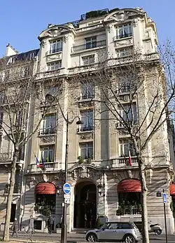A six-storey building at the corner of a terrace lined in front by bare trees