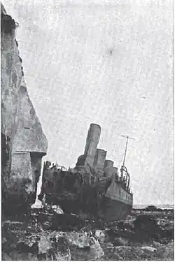 The destroyer HMS Nubian, beached near cliffs with her bow blown off by a torpedo.